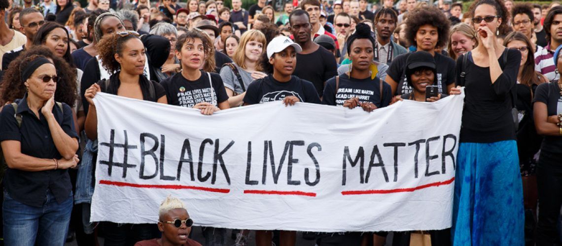 A large group of protesters, largely Black, holding a sign that says "Black Lives Matter"