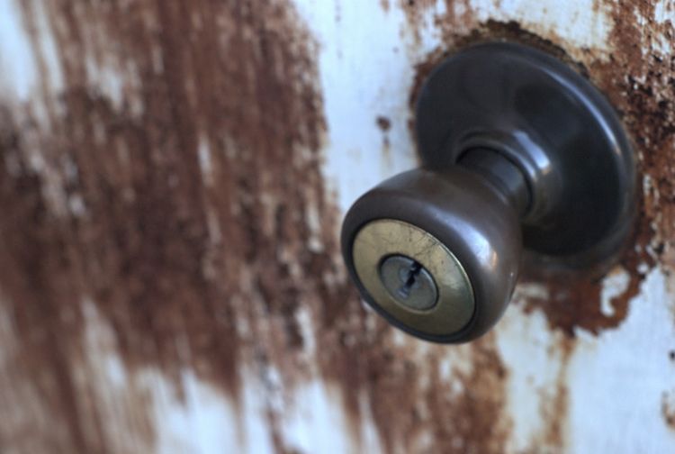 A close-up image of a brown doorknob on a rusty door.