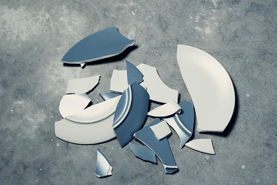 A dark blue and white plate, broken into pieces on a gray floor.